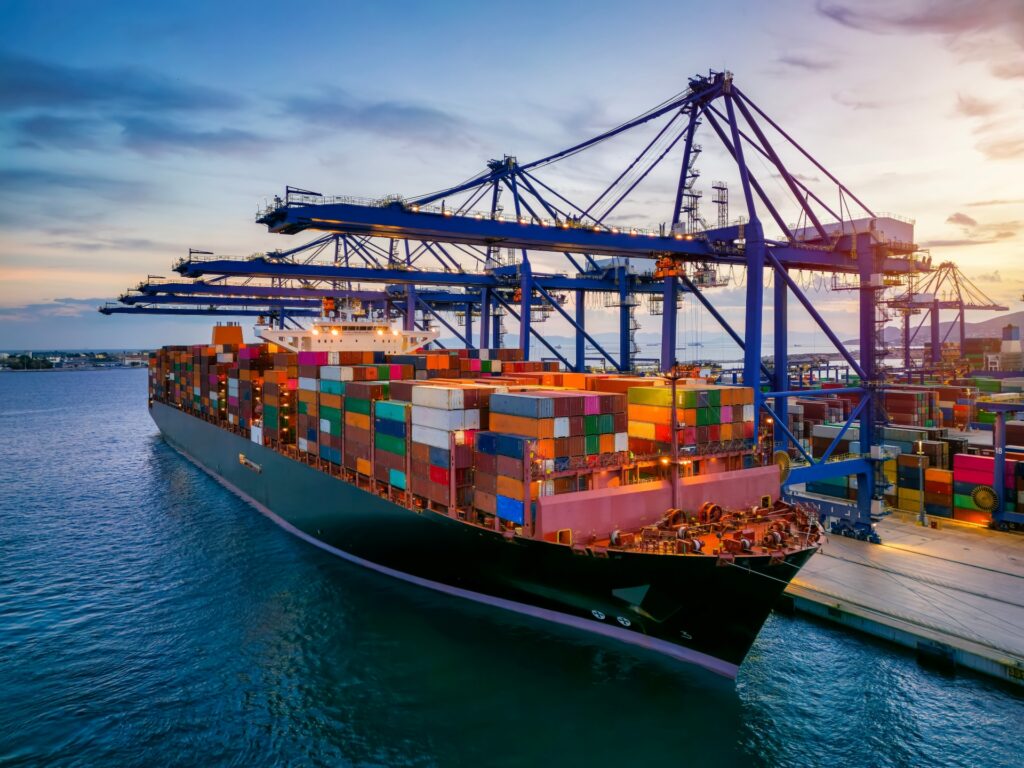 A large container ship docked at a busy port terminal, with colorful shipping containers stacked on board and cranes unloading cargo, illustrating global trade operations governed by Incoterms.